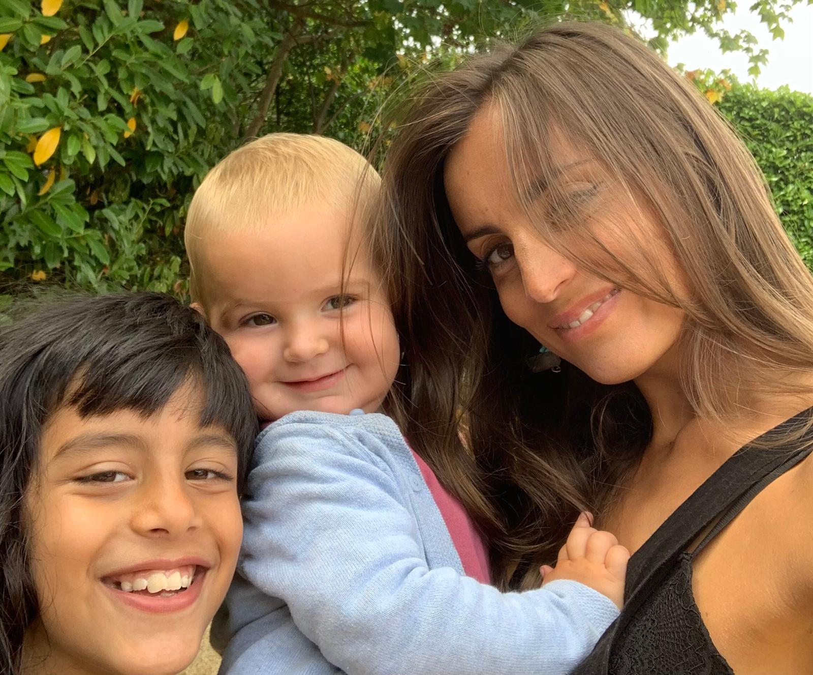 Daniella smiling with one of her own children outdoors in a garden